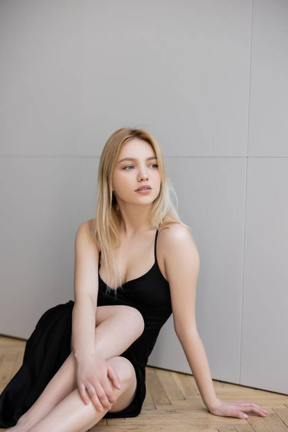 Elegant blonde woman in black dress sitting on floor at home  - 写真・画像
