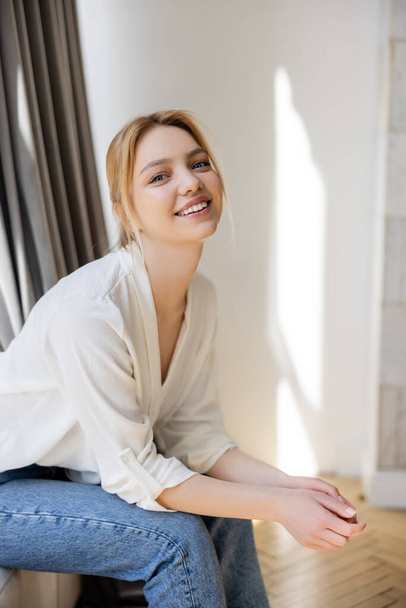Happy woman in jeans and blouse looking at camera at home  - Foto, Imagen