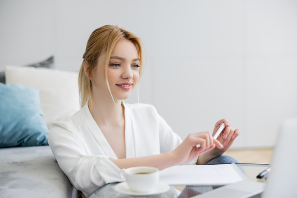Pretty freelancer looking at blurred laptop near cup and notebook at home  - Photo, Image
