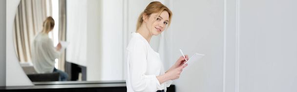 Femme blonde souriant à la caméra et écrivant sur un carnet à la maison, bannière  - Photo, image