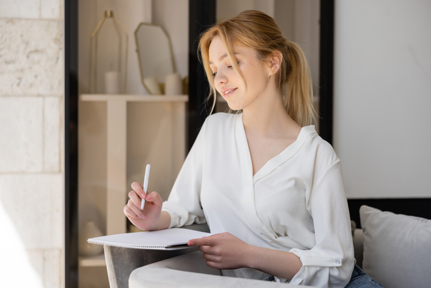 Femme blonde en chemisier tenant stylo et carnet à la maison  - Photo, image
