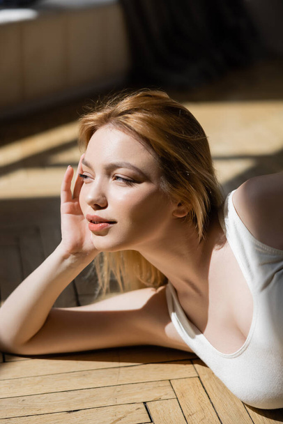 Portrait of young blonde woman looking away while lying on wooden floor  - Photo, image