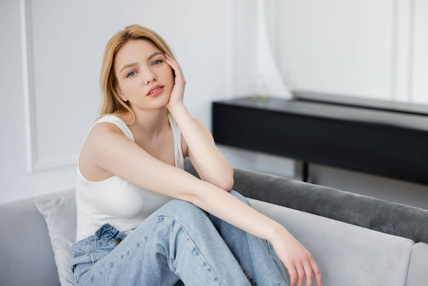 Kaunis blondi nainen farkut istuu sohvalla kotona  - Valokuva, kuva