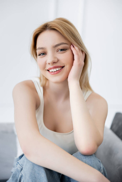 Portrait of positive young woman looking at camera on blurred couch  - Foto, Imagem