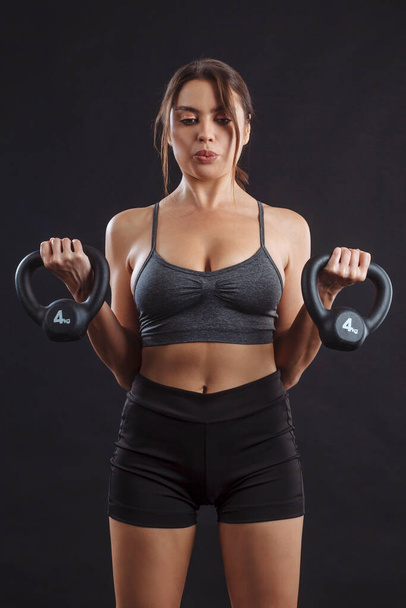 Young sexy woman exercising and doing bicep curls with a kettle bells. - 写真・画像