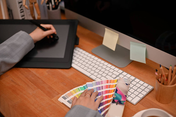 Professionelle Webgrafikerin sitzt an ihrem Schreibtisch im Büro, bedient sich eines Grafik-Tablets, untersucht Farbmuster-Diagramme und arbeitet an ihrem Projekt. Ansicht von oben - Foto, Bild