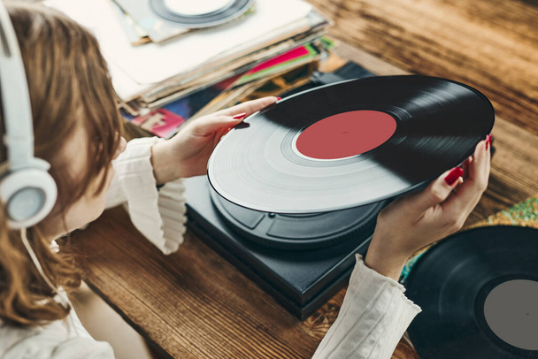 Young woman listening to music from vinyl record player. Playing music on turntable player. Female enjoying music from old record collection at home. Stack of analog vinyl records. Retro and vintage music style. Music Passion and hobby - Zdjęcie, obraz