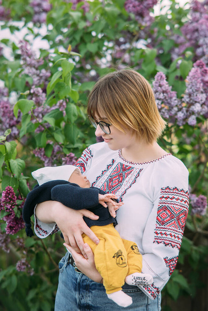 ウクライナの民族刺繍のシャツを着た幸せな白人女性は、異人種間の結婚から生まれたばかりの赤ちゃんを保持しています。異人種間の家族と団結の概念. - 写真・画像