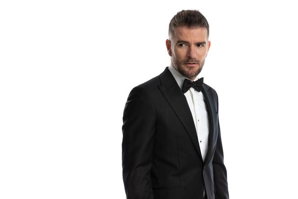 attractive businessman looking away and wearing a cool tuxedo against white background - Photo, Image