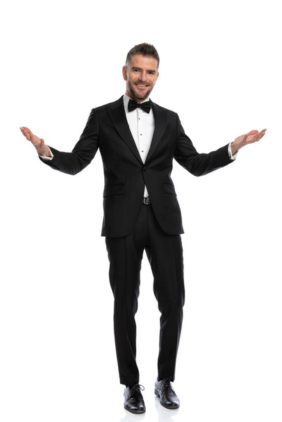 young smart casual man greeting the guests with open arms and smiling wide against white background - Photo, Image