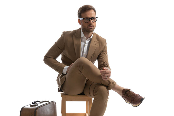 aantrekkelijke zakenman poseren op een stoel met zijn benen gekruist, weg te kijken en het dragen van een bril - Foto, afbeelding