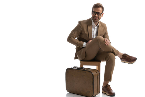 komea liikemies, jolla on hauskaa poseeraa tuolilla jalat ristissä, matkatavaroiden vieressä - Valokuva, kuva