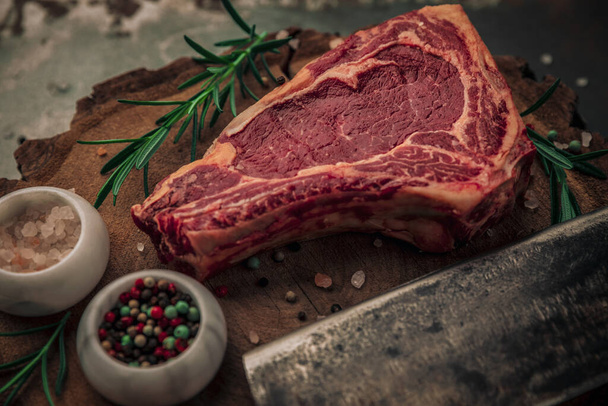 concept alimentaire de steak de boeuf cru avec romarin, sel et poivre et couteau de coupe sur le dessus de la planche à découper en bois  - Photo, image