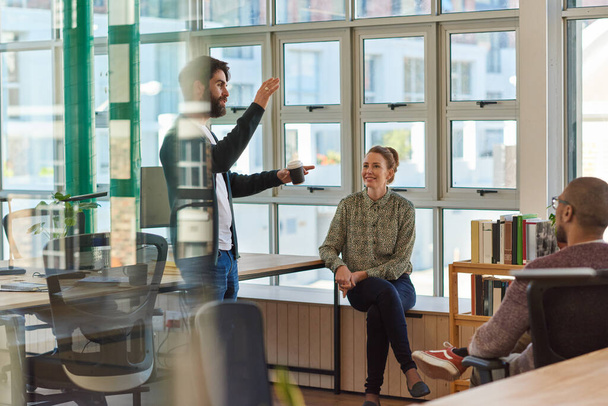 Young businessman talking with a group of colleagues during a casual meeting together inside of a modern office - Foto, Bild