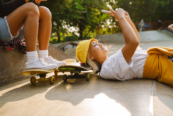 Asian girl laughing and using mobile phone while lying at skate park outdoors - Foto, imagen