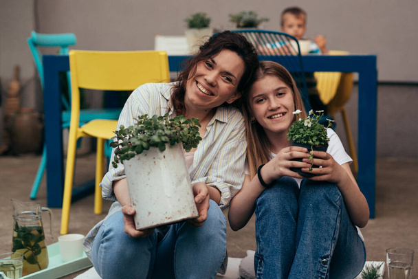 happy smiling mother and daughter holding houseplants and looking at camera - Фото, зображення