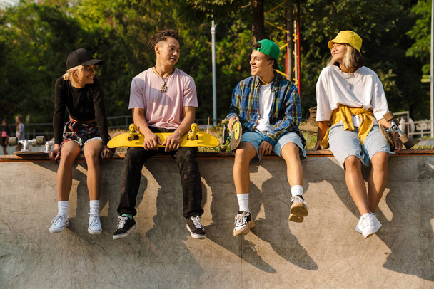 Multiracial teenagers talking and laughing while spending time at skate park outdoors - Фото, изображение