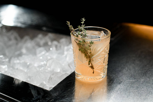 Selective focus on rosemary branch which garnished crystal glass of tasty cold cocktail. Blurred background - 写真・画像