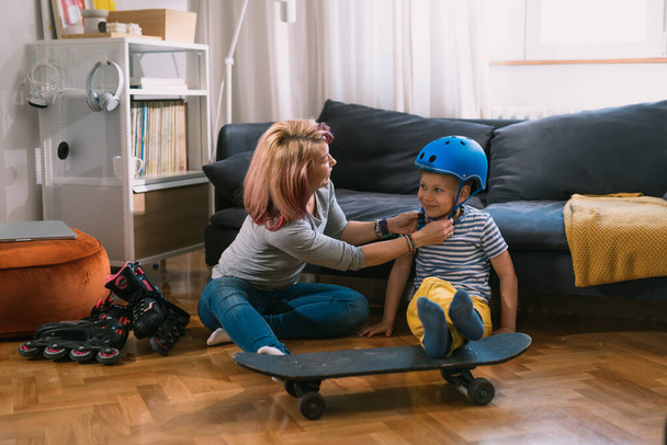 mother and son preparing for driving skateboard and rollerblade . they are in the living room - Photo, Image