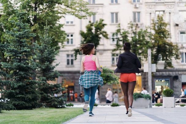 Visão traseira de amigos em sportswear correndo na cidade dicussing. Mulheres multiétnicas fazendo um exercício de fitness. - Foto, Imagem