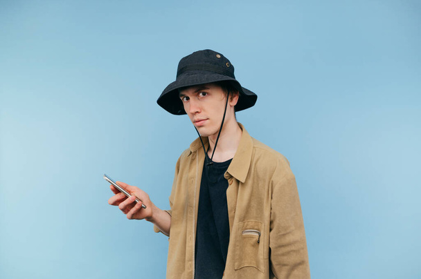 Concentrato giovane uomo in panama e camicia gode di smartphone con volto serio guardando la fotocamera - Foto, immagini