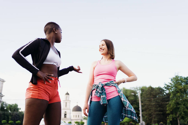 Ami souriant joyeux en vêtements de sport marchant après une séance de sport dans la ville discuter et s'amuser. Femmes multiethniques ayant un entraînement de fitness jogging. - Photo, image