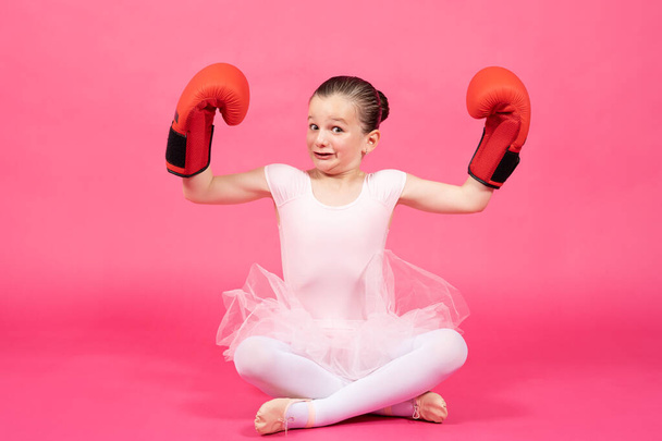 Pequeña bailarina clásica orgullosa mostrando bíceps y usando guantes de boxeo con cara divertida. Concepto de estereotipos femeninos. - Foto, Imagen