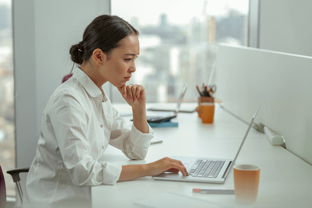 Focalizzato asiatico business donna lavoro laptop seduta in ufficio moderno. Foto di alta qualità - Foto, immagini