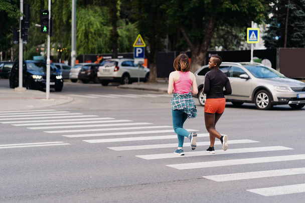 Amigos em sportswear correndo na cidade dicussing na rua pedonal. Mulheres multiétnicas fazendo um exercício de fitness. - Foto, Imagem