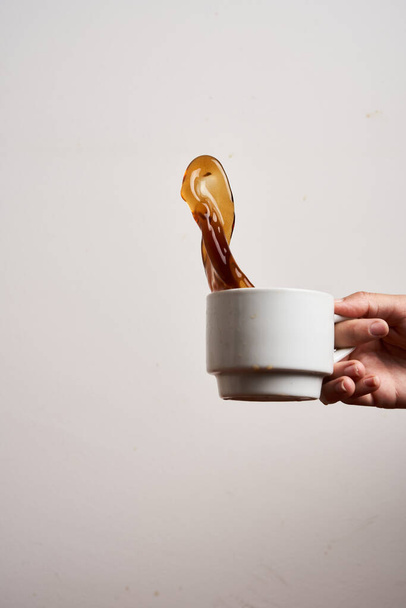 Mano de mujer sosteniendo una taza de café creando un chapoteo de café sobre fondo blanco. Aislado sobre blanco - Foto, Imagen