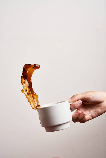 Main de femme tenant une tasse de café créant un éclaboussure de café sur fond blanc. Isolé sur blanc - Photo, image