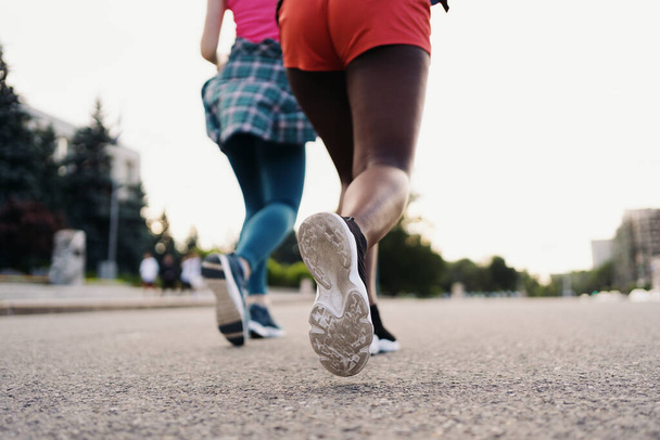 Visszapillantás a barátok lábára a városban futó sportruházatban. Többnemzetiségű, fitnesz edzéssel rendelkező nők. - Fotó, kép