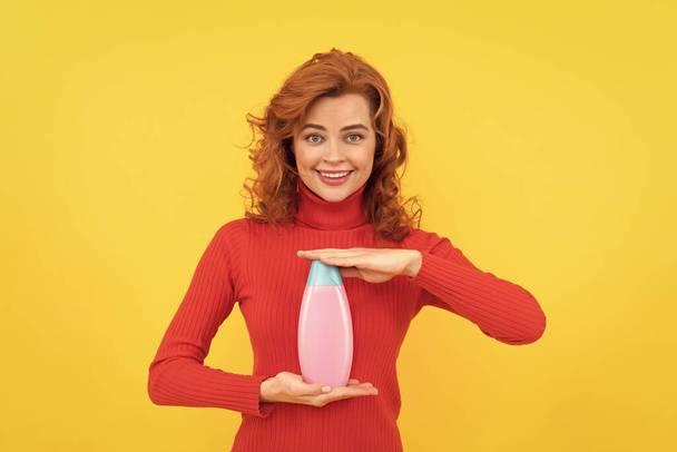 wesoła ruda kobieta kręcone farbowane włosy prezentujące produkt do pielęgnacji ciała szampon, reklama. - Zdjęcie, obraz