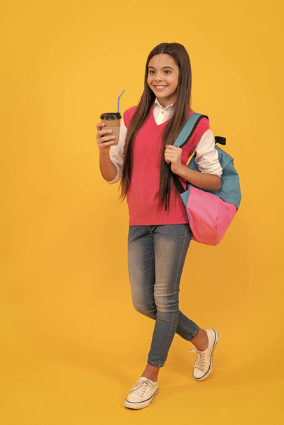 χαρούμενη έφηβη μαθήτρια με σακίδιο ποτό takeaway κακάο σε κίτρινο φόντο, μεσημεριανό γεύμα. - Φωτογραφία, εικόνα