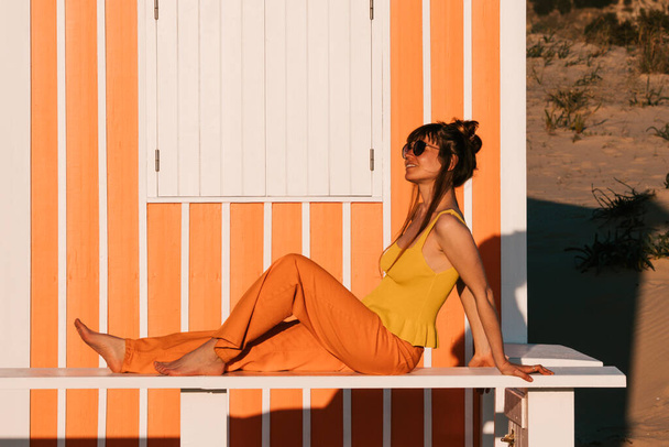 Молода жінка в жовтому баку зверху і апельсин, що стоїть ще біля апельсинового пляжного будинку
. - Фото, зображення