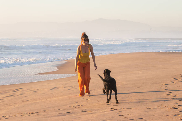 Beautiful woman fooling around with a dog in ocean beach. - 写真・画像
