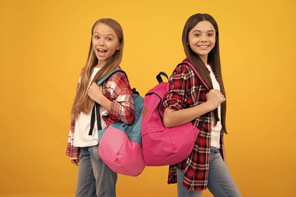 happy teen girls carry backpack. back to school. knowledge day. concept of education. kids with long hair on yellow background. september 1. happy childhood. children with school bag. - Photo, Image