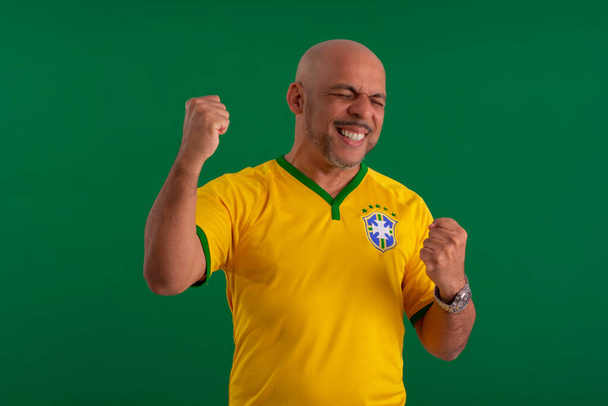 Afro Brésilien, supporter de l'équipe brésilienne de football dans la coupe 2022, avec le drapeau du Brésil et avec des expressions du visage. - Photo, image