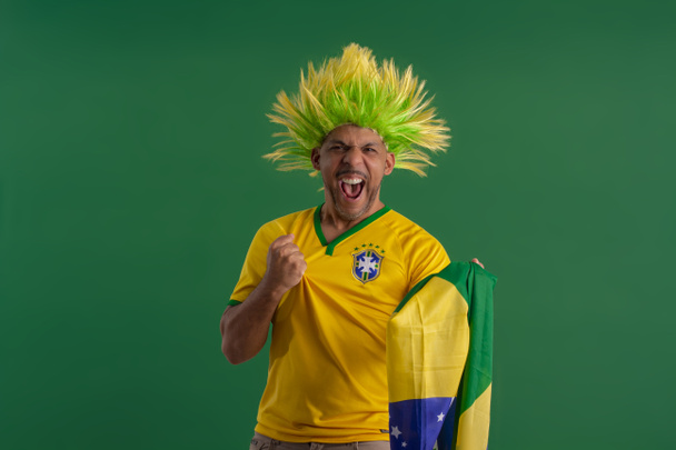 Homem afro-brasileiro, torcedor da Seleção Brasileira de Futebol na Copa 2022, com bandeira do Brasil e com expressões faciais. - Foto, Imagem