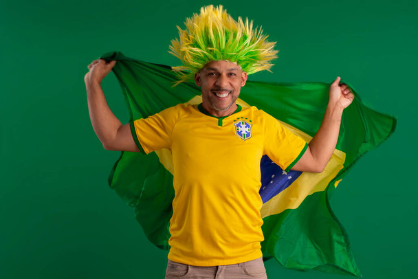 Афро-бразилец, болельщик бразильской футбольной команды в кубке 2022 года, с флагом Бразилии и выражением лица. - Фото, изображение