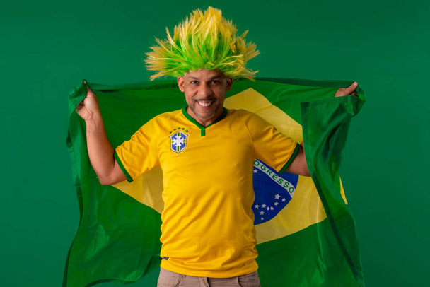 Afro Braziliaanse man, supporter van het Braziliaanse voetbalteam in de 2022 Cup, met de vlag van Brazilië en met gezichtsuitdrukkingen. - Foto, afbeelding
