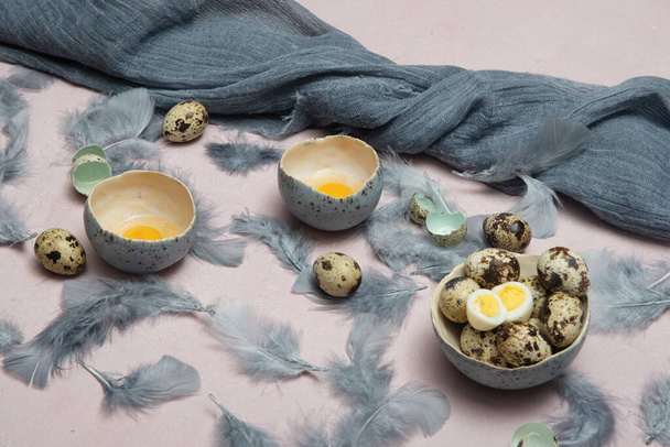 křepelčí vejce v keramických váz, šedé peří na stole, velikonoční zátiší, přírodní potraviny, strava a antioxidanty, tmavý klíč a mělká hloubka pole. Kvalitní fotografie - Fotografie, Obrázek