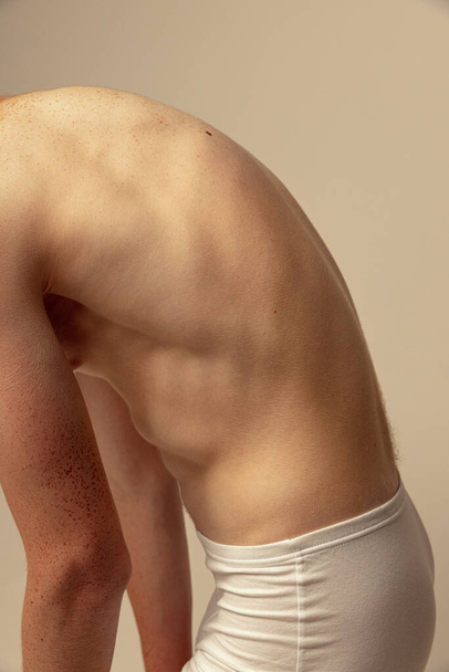 Обрезанное изображение мужской спины, мышечный рельеф изолирован на сером фоне студии. Модель позирует без рубашки, в нижнем белье. Веснушчатое тело. Концепция мужской красоты, моды, мужского здоровья, здоровья, фитнеса - Фото, изображение