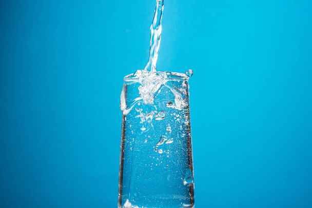 L'eau est versée dans un verre sur un fond bleu. Eau potable pure. - Photo, image