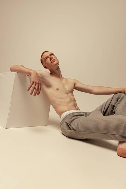 Portrait of young handsome red-haired man posing shirtless in pants isolated over grey studio background. Concept of male beauty, fashion, mens health, wellness, fitness. Dreamy look - Φωτογραφία, εικόνα