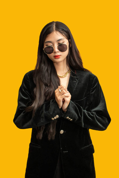 Modekonzept: Modische Frau trägt Sonnenbrille und Oversize-Mantel, um auf gelbem Hintergrund zu posieren. - Foto, Bild