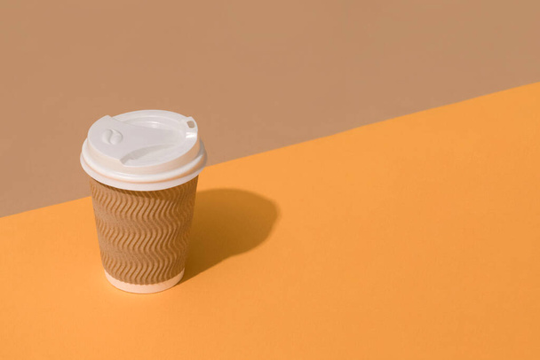 Mockup obrázek hnědé kraft papírový šálek kávy s bílým plastovým víčkem přes oranžové a hnědé pozadí s kopírovacím prostorem. Udržitelná koncepce balení potravin - Fotografie, Obrázek
