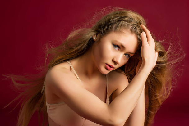 Hermosa modelo chica con el pelo largo y rubio. Fondo rojo. Productos para el cabello cuidado y belleza. Moda, cosméticos y maquillaje. - Foto, Imagen