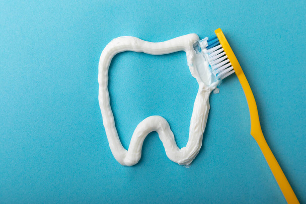 Tooth symbol made from toothpaste and a toothbrush on a blue background. Refreshing and whitening toothpaste. Copy space for text. Flat lay. Prevention of caries. The concept of teeth cleaning. - Photo, Image