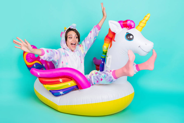 Photo of adorable funky young woman dressed unicorn nightwear smiling riding bloated circle isolated teal color background. - Zdjęcie, obraz